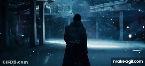 A Man Is Standing In A Dark Room With Snow Falling . GIF