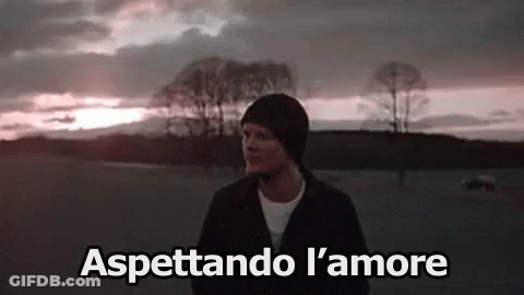 A Man Is Standing In A Field With Trees In The Background And The Words Aspettando L ' Amore Above Him . GIF