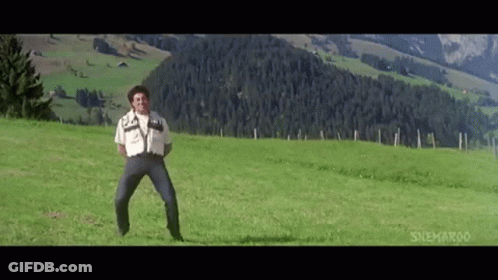 A Man Is Standing In A Grassy Field In Front Of A Mountain . GIF