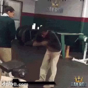 A Man Is Standing In A Gym In Front Of A Sign That Says Ray Rod . GIF
