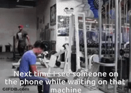 A Man Is Standing In A Gym Looking At His Phone GIF