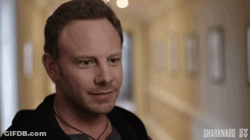 A Man Is Standing In A Hallway Smiling And Looking At The Camera . GIF