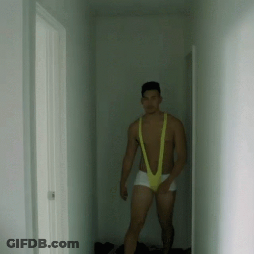 A Man Is Standing In A Hallway Wearing A Yellow Slingshot Underwear . GIF