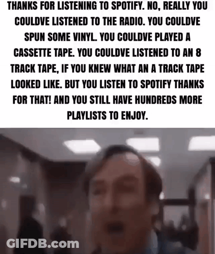 A Man Is Standing In A Hallway With A Spotify Playlist On His Phone . GIF