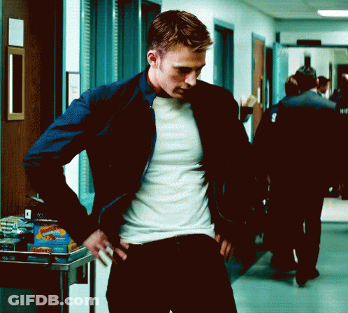 A Man Is Standing In A Hallway With His Hands On His Hips Wearing A White Shirt And A Blue Jacket . GIF