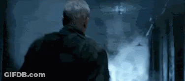 A Man Is Standing In A Hallway With Smoke Coming Out Of The Door . GIF