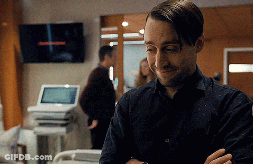 A Man Is Standing In A Hospital Room With His Arms Crossed And Smiling GIF