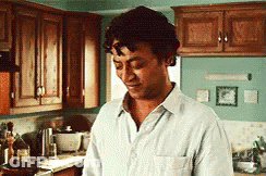 A Man Is Standing In A Kitchen Looking Down At Something GIF