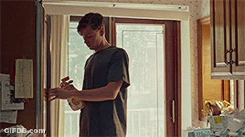 A Man Is Standing In A Kitchen Next To A Window . GIF