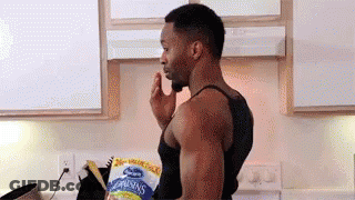 A Man Is Standing In A Kitchen With A Bag Of Raisins In His Hand . GIF