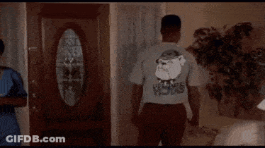 A Man Is Standing In A Living Room Wearing A T-Shirt With A Picture Of Santa Claus On The Back . GIF