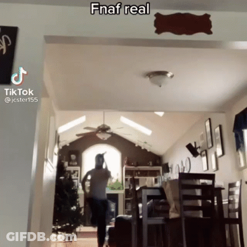 A Man Is Standing In A Living Room With A Ceiling Fan And A Sign On The Wall That Says Fnaf Real . GIF