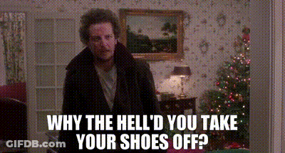 A Man Is Standing In A Living Room With A Christmas Tree In The Background And A Picture On The Wall . GIF