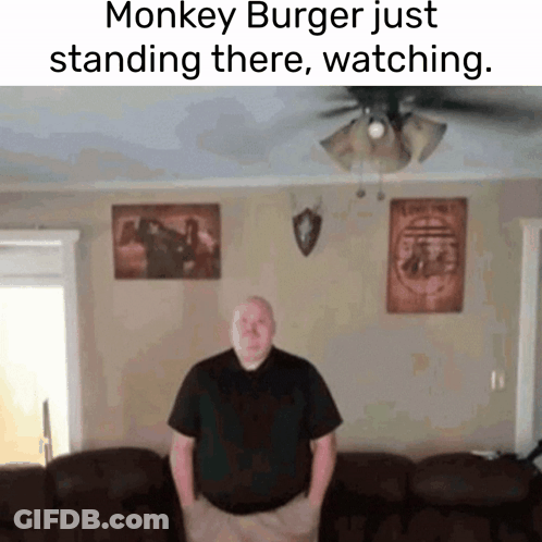 A Man Is Standing In A Living Room With A Monkey Burger Just Standing There Watching GIF