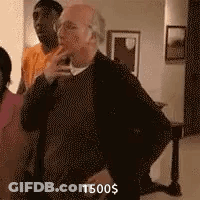 A Man Is Standing In A Living Room With A Woman And A Man Standing Behind Him . GIF