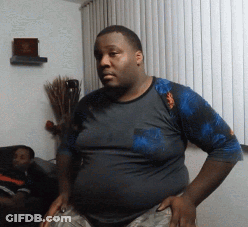 A Man Is Standing In A Living Room With His Hands On His Hips While Another Man Sits On A Couch . GIF