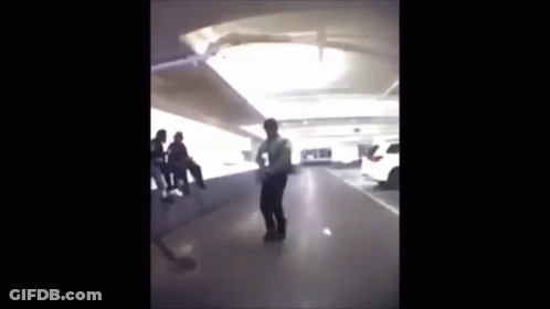 A Man Is Standing In A Parking Garage With A Group Of People Sitting On A Bench . GIF