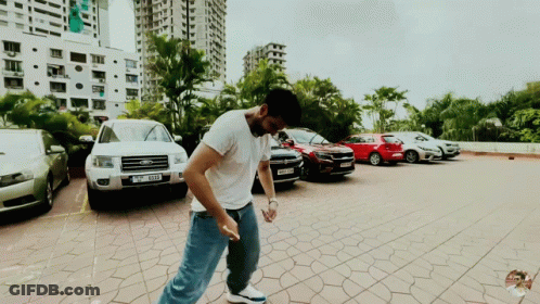 A Man Is Standing In A Parking Lot With A Ford Car Parked Behind Him GIF