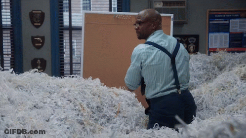 A Man Is Standing In A Pile Of Shredded Paper In Front Of A Bulletin Board That Says News Of New York GIF