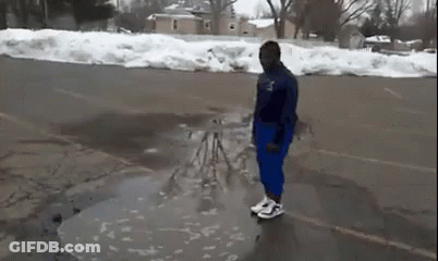 A Man Is Standing In A Puddle Of Water On The Side Of A Road . GIF