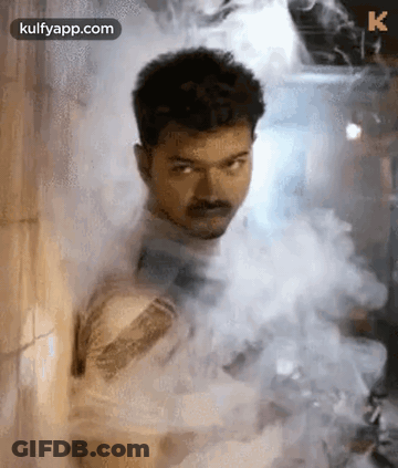A Man Is Standing In A Room Covered In Smoke . GIF