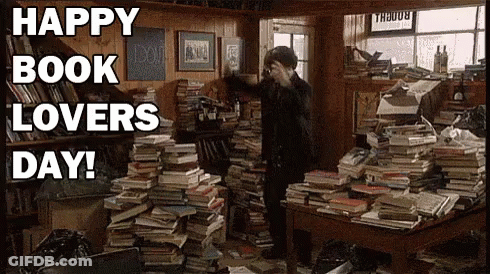 A Man Is Standing In A Room Filled With Lots Of Books And A Sign That Says Happy Book Lovers Day . GIF