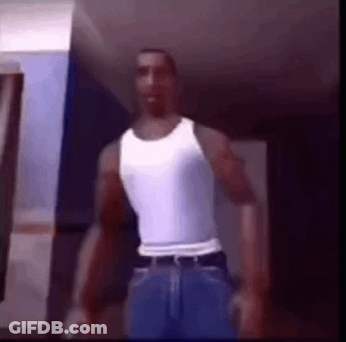 A Man Is Standing In A Room Wearing A White Tank Top And Blue Jeans . GIF
