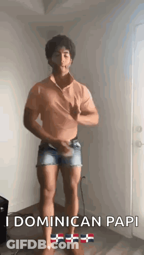 A Man Is Standing In A Room Wearing Shorts And A Shirt That Says Dominican Papi . GIF