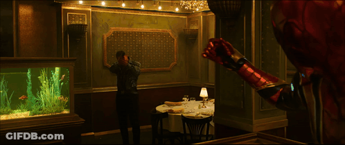A Man Is Standing In A Room With A Table And A Lamp GIF