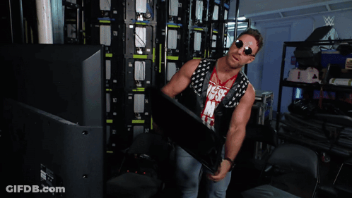 A Man Is Standing In A Room With A Wrestling Logo On The Wall GIF