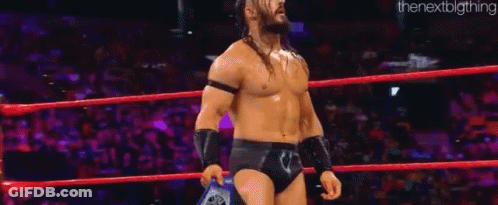 A Man Is Standing In A Wrestling Ring Holding A Championship Belt . GIF
