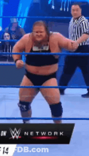 A Man Is Standing In A Wrestling Ring With A Referee Behind Him . GIF