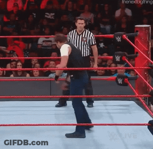 A Man Is Standing In A Wrestling Ring With A Referee In The Background . GIF