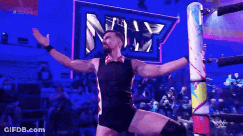 A Man Is Standing In A Wrestling Ring With His Arms Outstretched In Front Of A Crowd . GIF