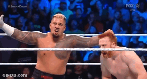 A Man Is Standing In A Wrestling Ring With His Arms Outstretched Next To Another Man . GIF
