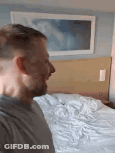 A Man Is Standing In Front Of A Bed With A Picture On The Wall . GIF