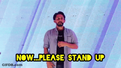 A Man Is Standing In Front Of A Blue Wall And Says Now Please Stand Up GIF