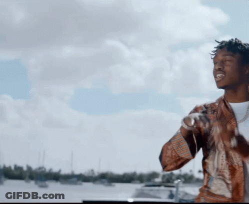 A Man Is Standing In Front Of A Body Of Water With Boats In The Background GIF