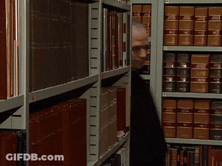 A Man Is Standing In Front Of A Bookshelf With A Book Titled ' A Brief History Of The World ' On It GIF