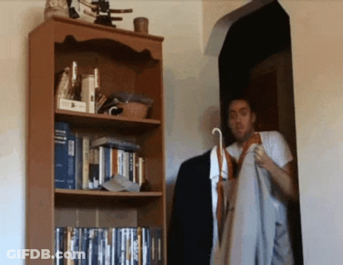 A Man Is Standing In Front Of A Bookshelf With A Book Titled ' A Dictionary ' On The Top Shelf GIF
