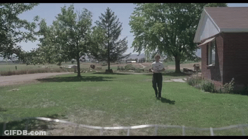 A Man Is Standing In Front Of A Brick House Holding A Piece Of Paper GIF