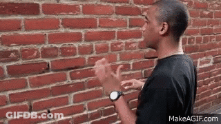 A Man Is Standing In Front Of A Brick Wall . GIF