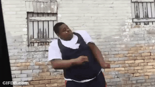 A Man Is Standing In Front Of A Brick Wall Dancing . GIF