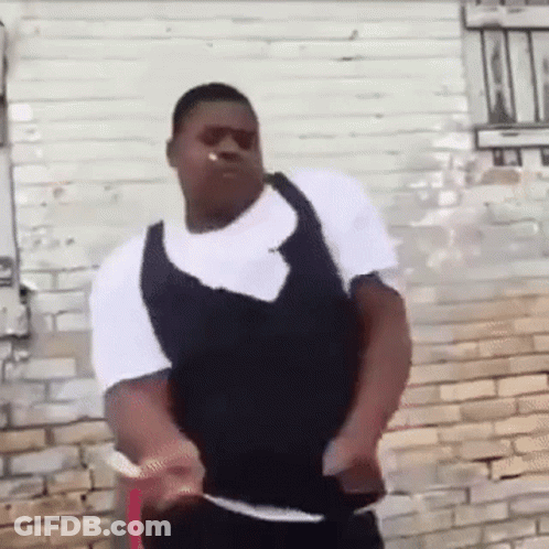 A Man Is Standing In Front Of A Brick Wall Wearing Sunglasses And A Vest . GIF