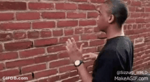 A Man Is Standing In Front Of A Brick Wall With His Hands Outstretched . GIF