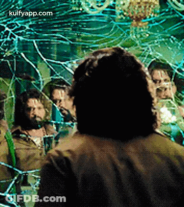 A Man Is Standing In Front Of A Broken Mirror With A Group Of People Behind Him . GIF