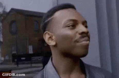 A Man Is Standing In Front Of A Building Looking At The Camera . GIF