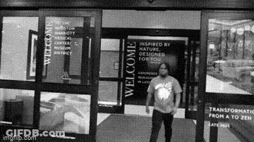 A Man Is Standing In Front Of A Building With A Welcome Sign On It . GIF