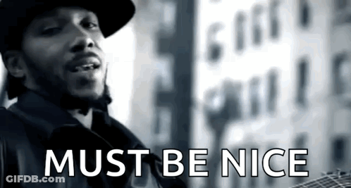A Man Is Standing In Front Of A Building With The Words Must Be Nice On The Bottom GIF