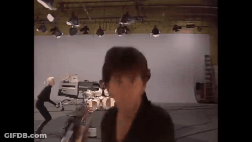 A Man Is Standing In Front Of A Camera In A Studio With A Drum Set In The Background . GIF